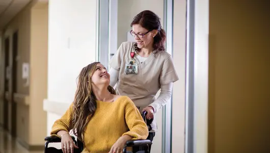 Female nurse pushing adult female patient in wheelchair.