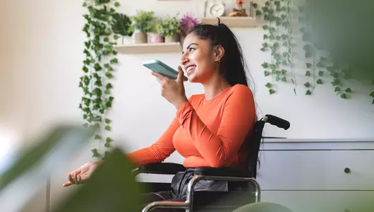 Smiling disabled woman in wheelchair, talking on mobile phone at home.