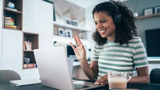 woman with headphones on waving at her computer