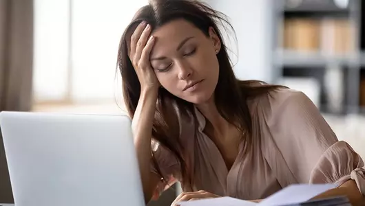 woman holding head in hand looking tired in front of computer