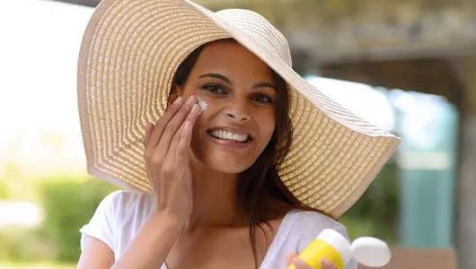 woman putting sunscreen on face while wearing big hat