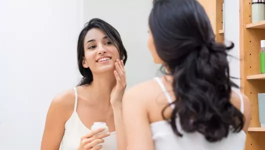 woman looking in mirror putting on moisturizer