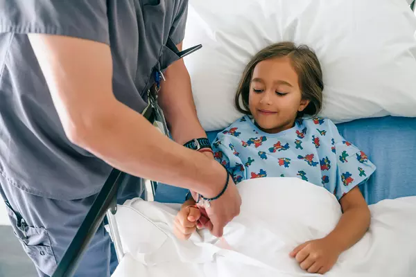 Doctor holding hand of girl in hospital bed.