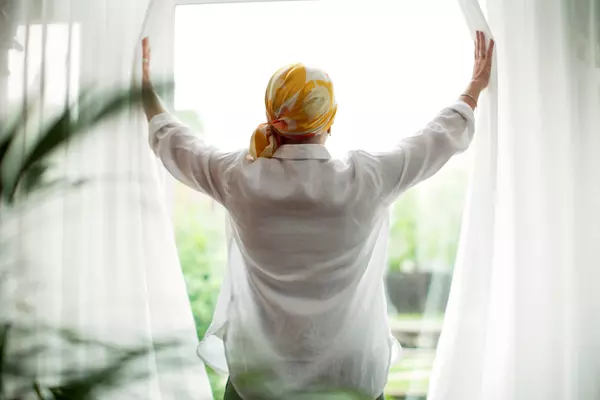Rear view of mature woman opening curtains at window