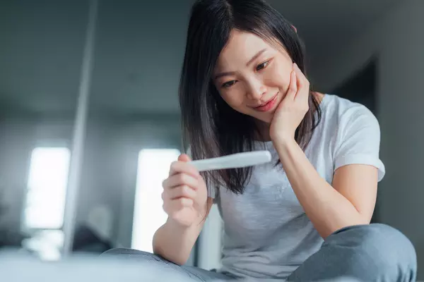 Young Asian woman holding home pregnancy test and looking cheerful.
