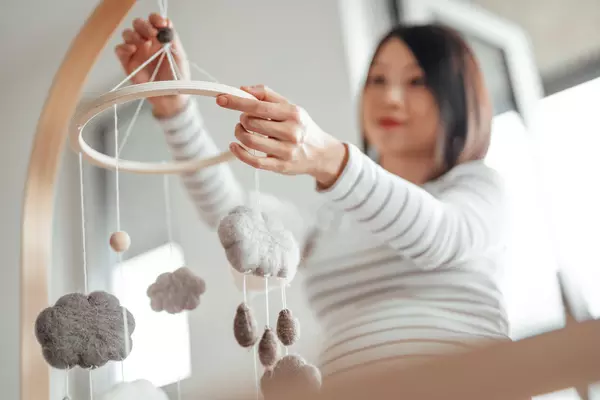 Close-up low angle view of Asian pregnant woman hanging a baby mobile onto a wooden crib.